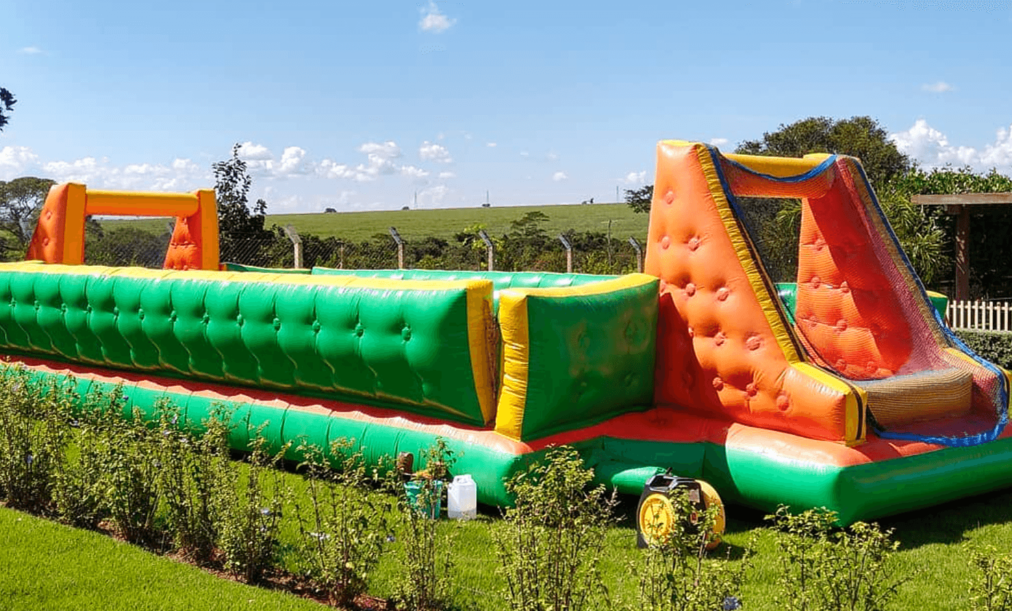Pista inflável gigante com escorregador montada no gramado sob céu azul